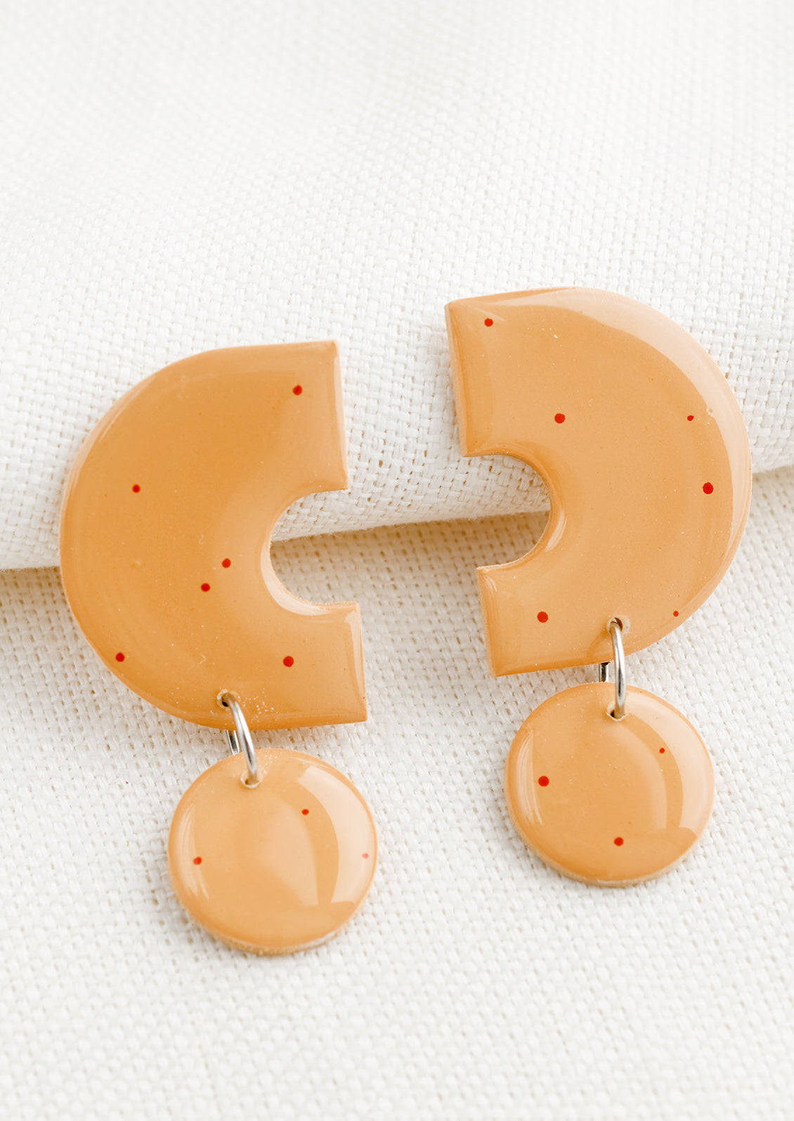 A pair of clay earrings with geometric shape in peach with red splatters.