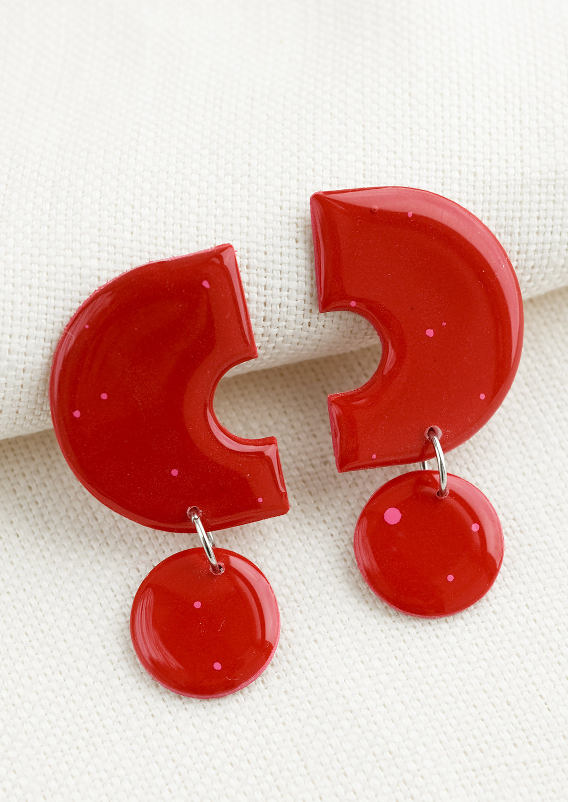 A pair of clay earrings with geometric shape in red with pink splatters.