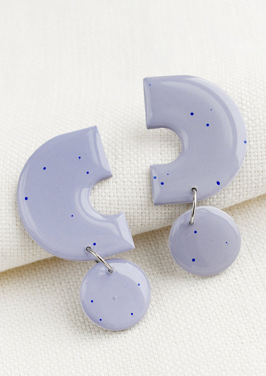 A pair of clay earrings with geometric shape in purple with blue splatters.