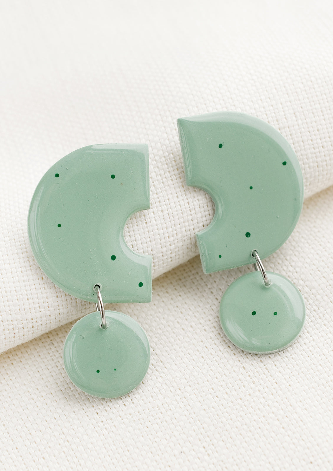 A pair of clay earrings with geometric shape in seafoam with green splatters.
